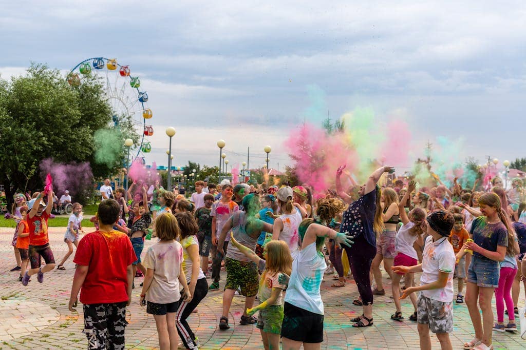 Vibrant outdoor festival with children and adults throwing colorful powders in a lively atmosphere.